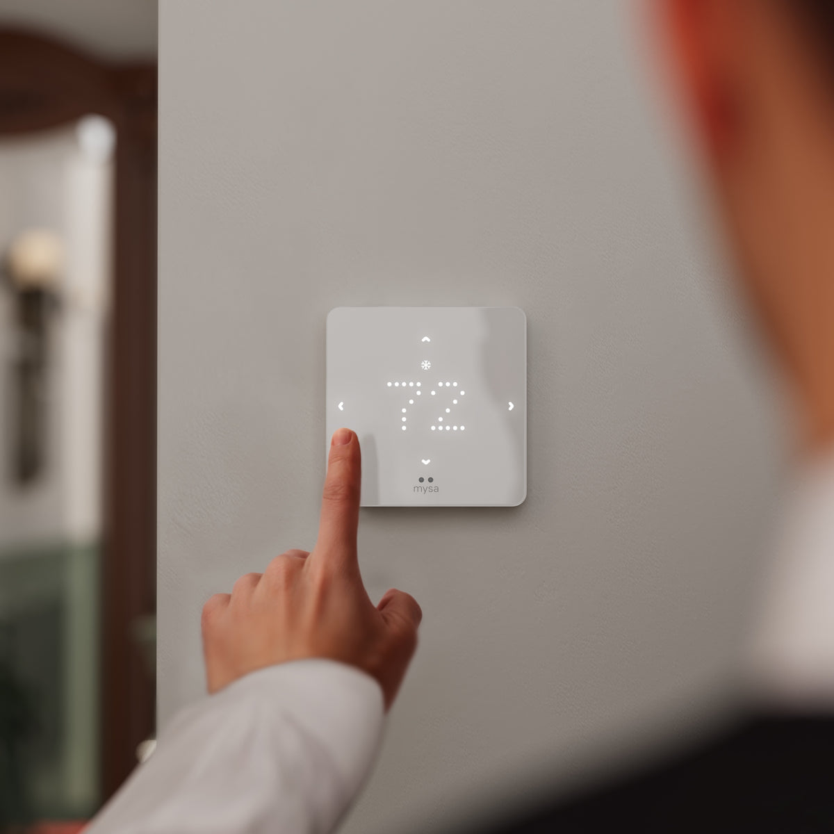 Person adjusting a digital thermostat on a wall